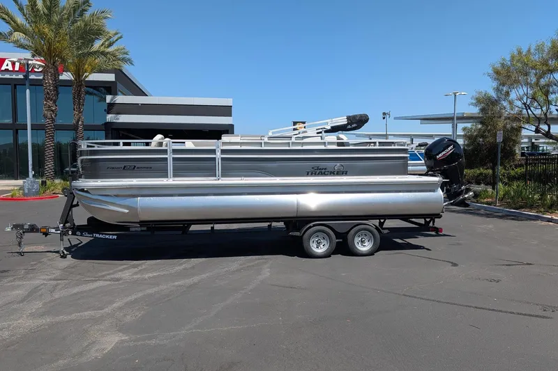 The Image of 2026 Sun Tracker Fishin' Barge 22 DLX pontoon boat on trailer in parking lot. - 0