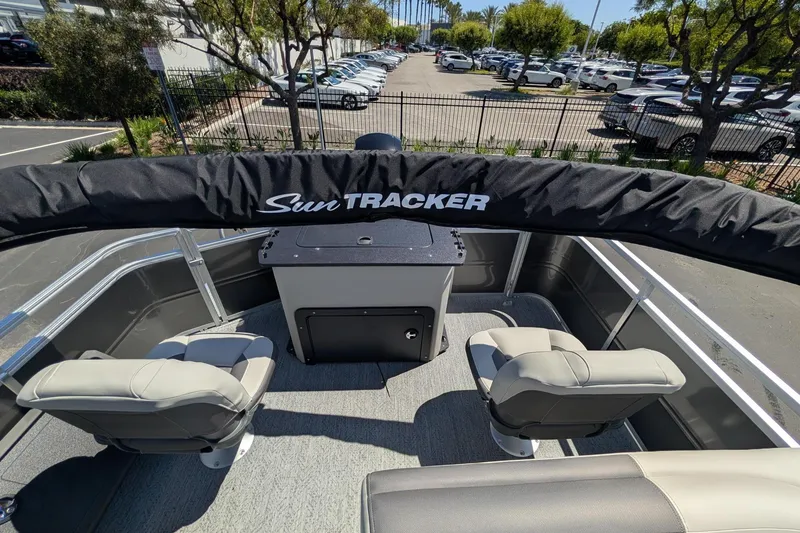 Slide: The Image of 2026 Sun Tracker Fishin' Barge 22 DLX interior with seating and storage, parked outdoors. - 10