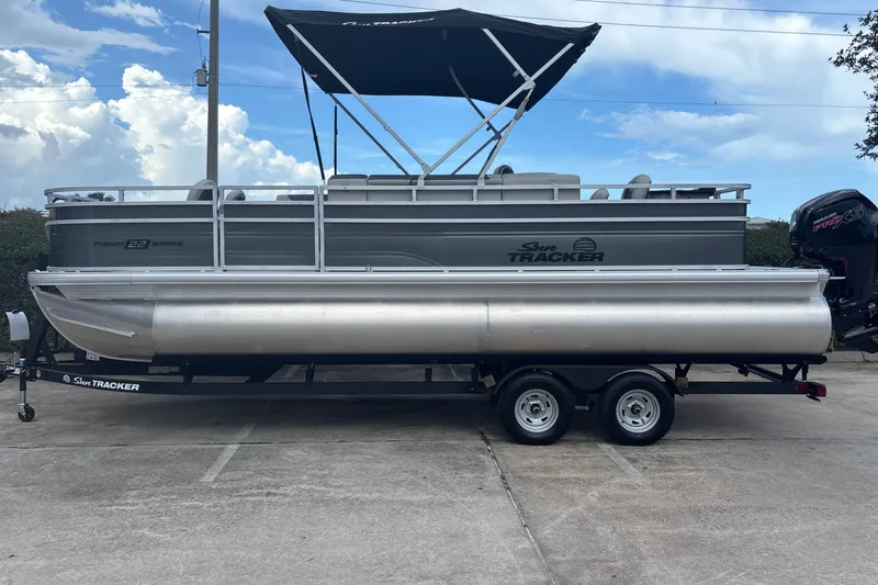 The Image of 2026 Sun Tracker Fishin' Barge 22 DLX pontoon boat on trailer, parked outdoors. - 0