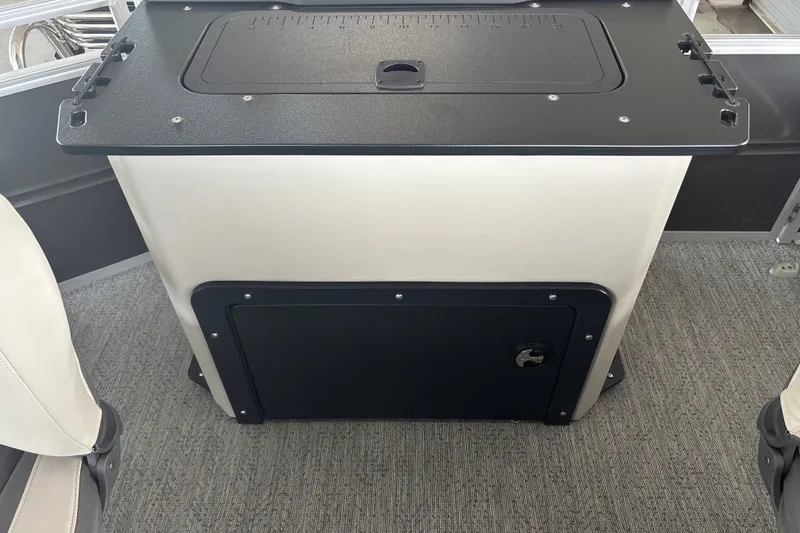 Slide: The Image of 2026 Sun Tracker Fishin' Barge 22 DLX storage compartment with black lid and carpeted floor. - 36