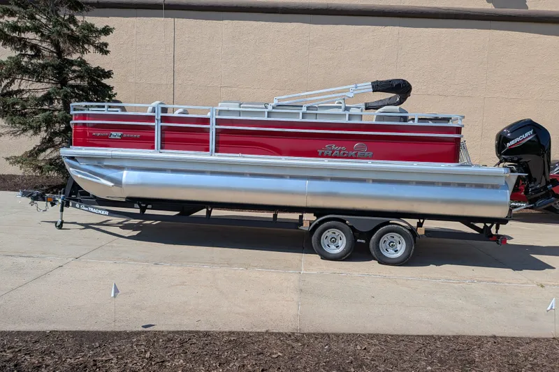 The Image of 2026 Sun Tracker Fishin' Barge 22 DLX pontoon boat on trailer, parked outdoors. - 0