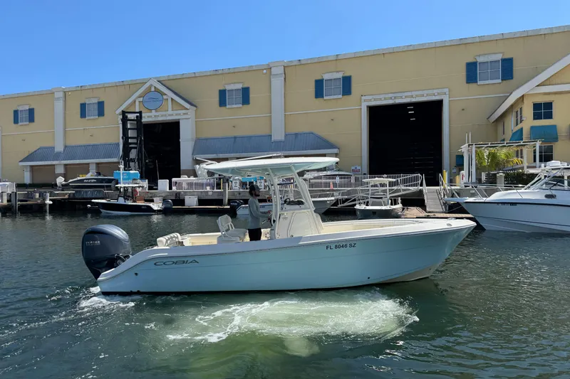 The Image of 2021 Cobia 237 Center Console boat docked near a marina warehouse. - 1