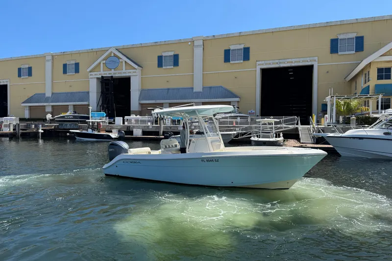 Slide: The Image of 2021 Cobia 237 Center Console boat docked near a marina warehouse. - 3