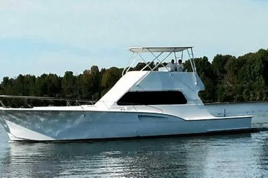The Image of 1976 Hatteras 53 Convertible yacht on calm water, surrounded by lush greenery. - 0