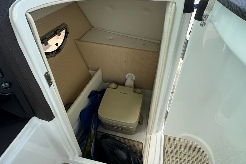 Slide: The Image of Compact cabin toilet in a 2018 Cobalt 23SC boat, featuring storage space and a small window. - 15
