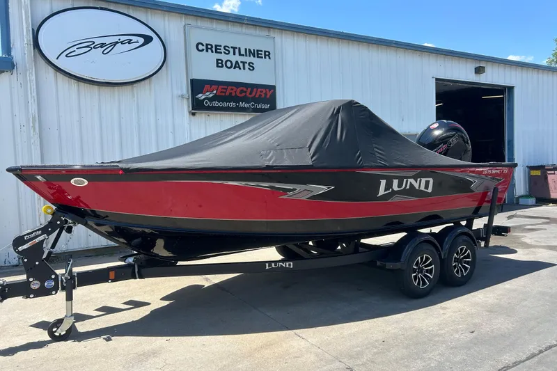 Slide: The Image of 2026 Lund 1875 Impact XS Sport boat, red and black, covered, on trailer outside dealership. - 8