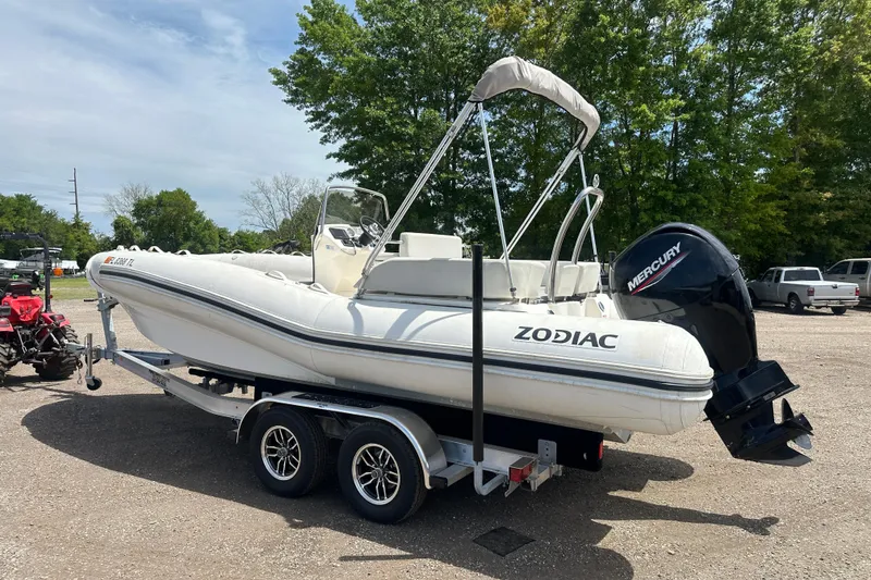 Slide: The Image of 2023 Zodiac N-ZO 680 boat on trailer with Mercury outboard motor, parked outdoors. - 2