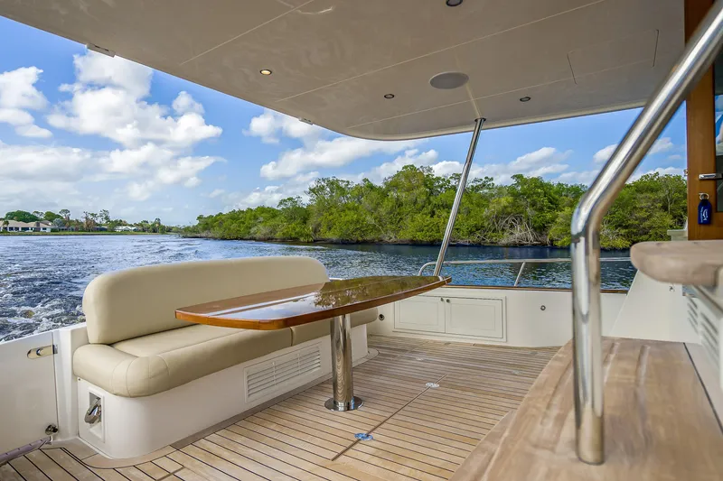 Slide: The Image of 2023 Grand Banks GB54 yacht deck with seating and table, cruising on a scenic waterway. - 11
