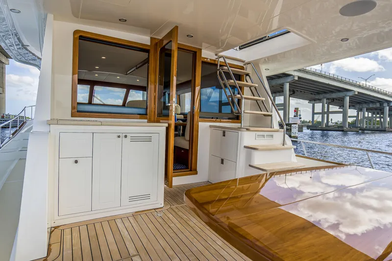 Slide: The Image of 2023 Grand Banks GB54 yacht deck with wooden table, cabinets, and stairs under a bridge. - 18