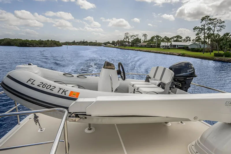 Slide: The Image of 2023 Grand Banks GB54 yacht with a small inflatable boat on deck, cruising on a scenic waterway. - 20