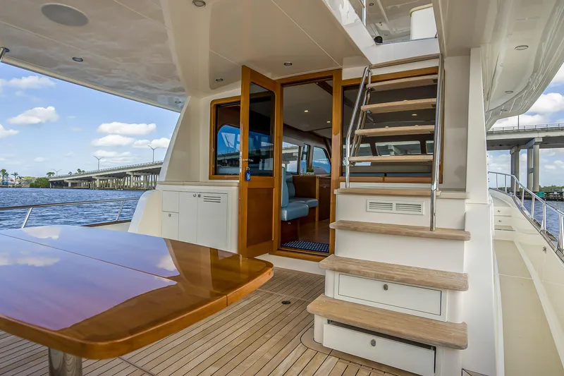 Slide: The Image of 2023 Grand Banks GB54 yacht deck with wooden table and stairs, near a bridge. - 9