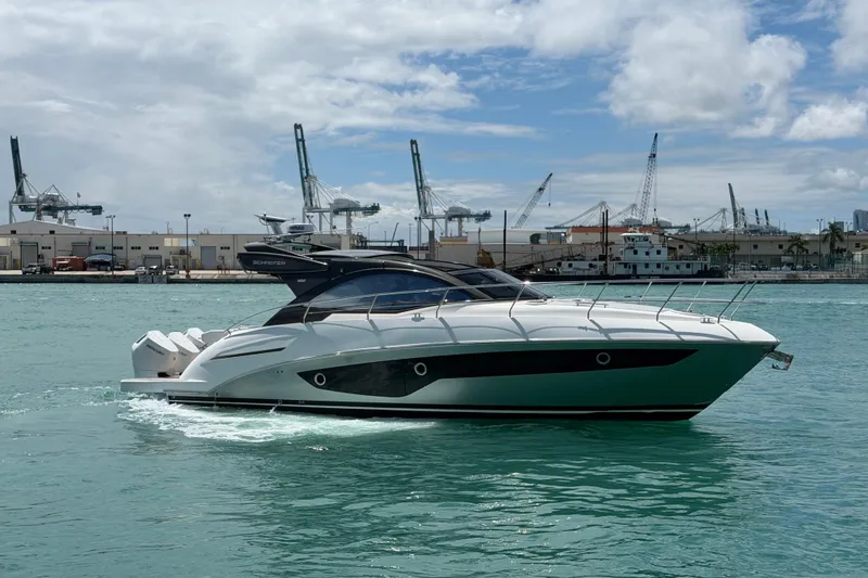 The Image of 2024 Schaefer 400 yacht cruising in a harbor with industrial cranes in the background. - 0