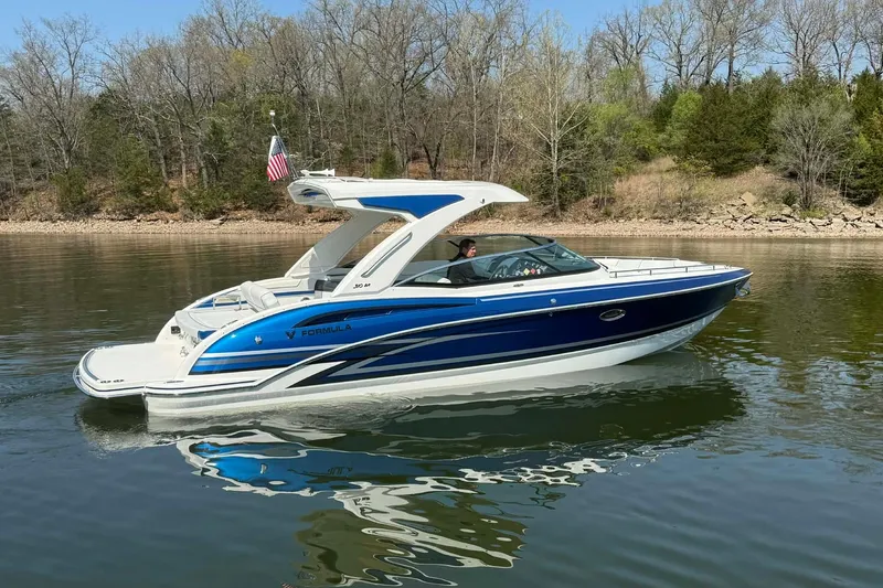 The Image of 2026 Formula 310 Bowrider I/O boat cruising on a calm lake with forested shoreline. - 0
