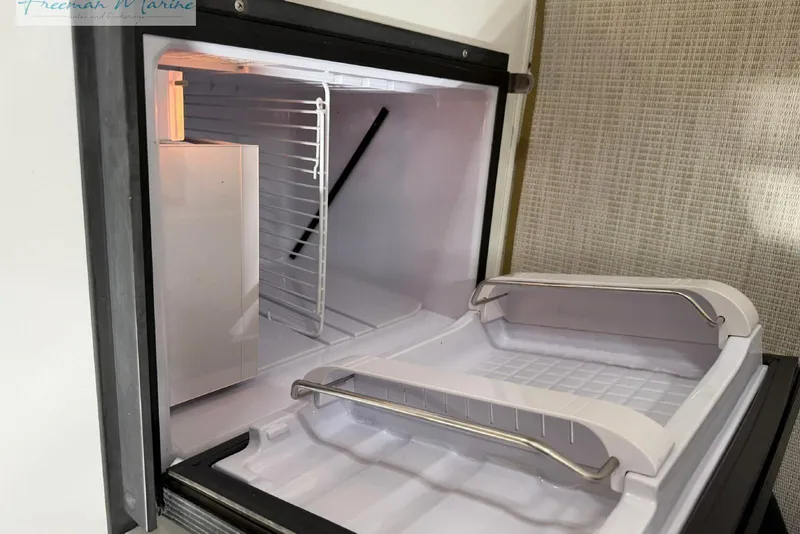 Slide: The Image of Open refrigerator in a 2016 Marker One M25 boat, showing empty shelves and interior light. - 11