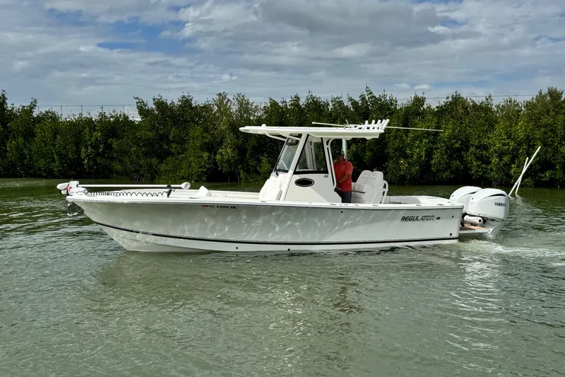 Slide: The Image of 2022 Regulator 28 boat cruising on calm water with lush greenery background. - 12