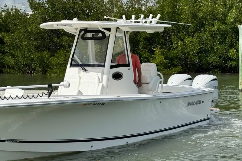 Slide: The Image of 2022 Regulator 28 boat cruising in calm waters near lush greenery. - 9