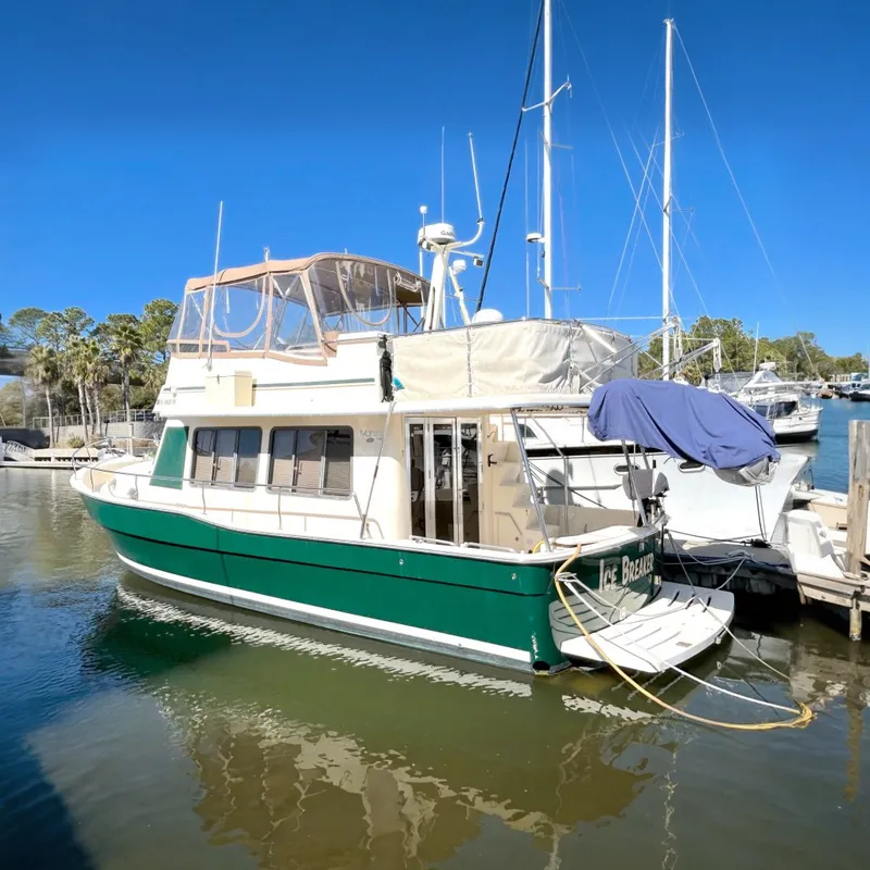 The Image of A 2004 Mainship 400 Trawler is docked in the water, surrounded by other boats. It has a green hull and white upper structure. - 0