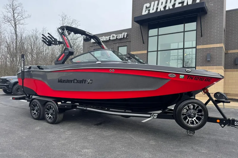The Image of 2022 MasterCraft XT24 boat in red and black, parked outside dealership. - 1