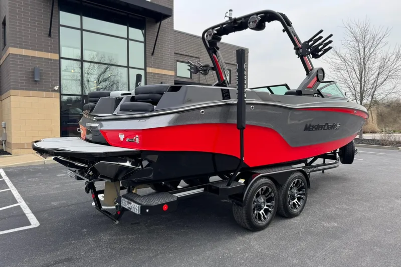 Slide: The Image of 2022 MasterCraft XT24 boat in vibrant red and gray on a trailer, parked outside a building. - 3