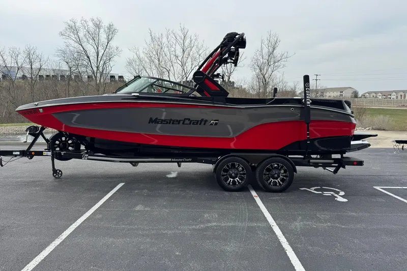 Slide: The Image of 2022 MasterCraft XT24 boat in red and gray on a trailer in a parking lot. - 5