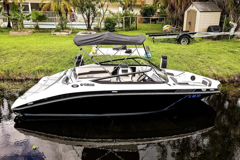 The Image of 2023 Yamaha Boats SX195 on trailer, parked near palm trees under cloudy sky. - 0
