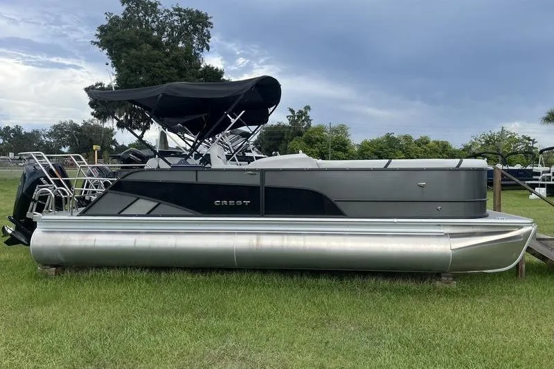 The Image of 2024 Crest Classic Platinum 240 SLC pontoon boat on grass, under cloudy sky. - 0