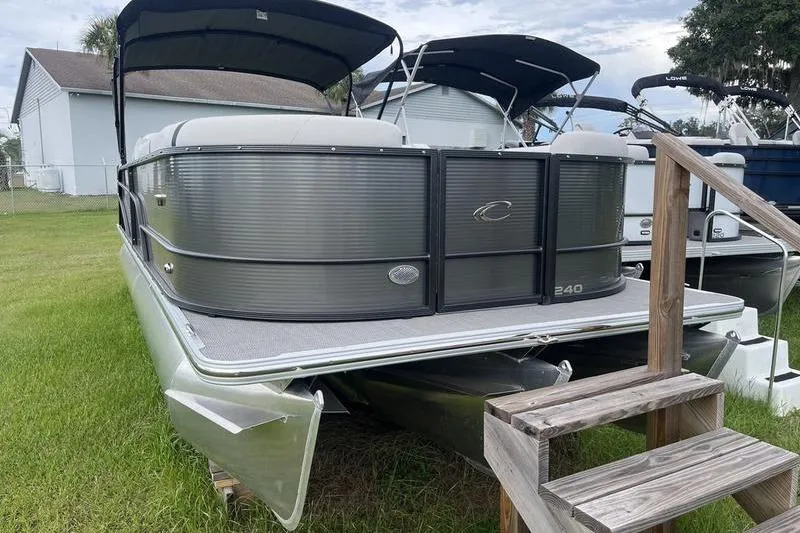 Slide: The Image of 2024 Crest Classic Platinum 240 SLC pontoon boat on grass with wooden steps. - 2