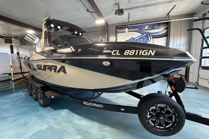 The Image of 2023 Supra SE 550 boat on trailer in showroom setting. - 1