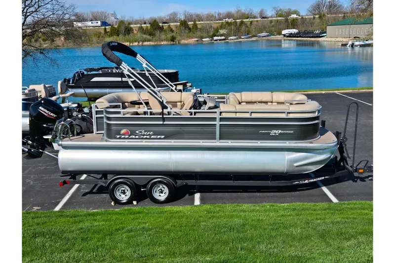 The Image of 2024 Sun Tracker Party Barge 20 DLX pontoon boat on trailer by a lake. - 0