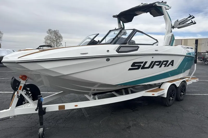 The Image of 2026 Supra SV boat on trailer, white and teal design, parked outdoors. - 1