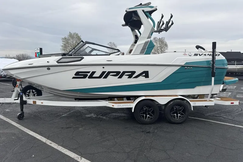 Slide: The Image of 2026 Supra SV boat on trailer, white and teal design, parked outdoors. - 2