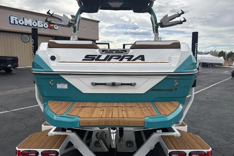 Slide: The Image of 2026 Supra SV boat with teal accents and wooden deck, parked outdoors. - 4