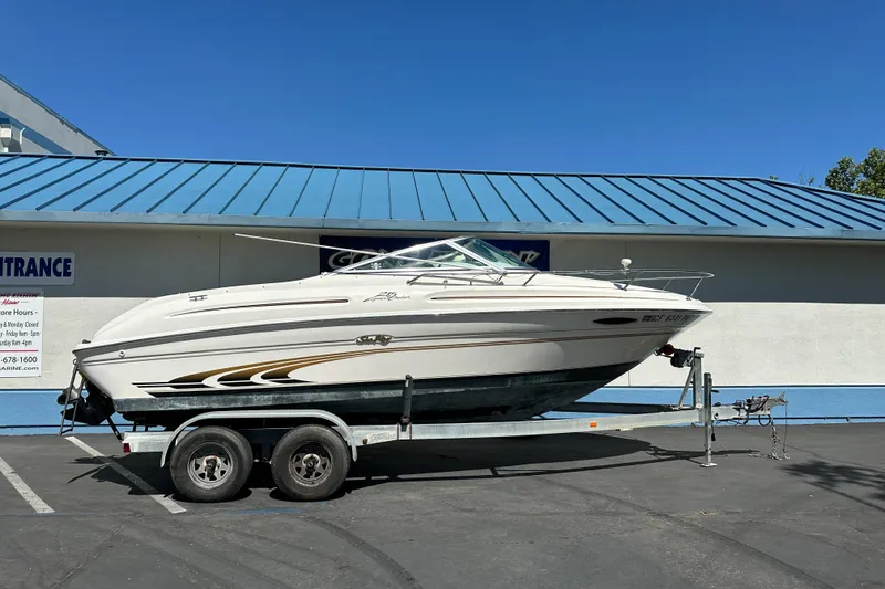 The Image of 1998 Sea Ray 215 Express Cruiser on trailer, parked outside a building with blue roof. - 1
