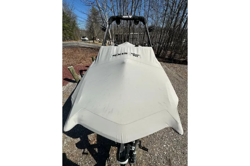 Slide: The Image of 2024 Axis A20 boat covered, parked outdoors on gravel, surrounded by trees. - 29