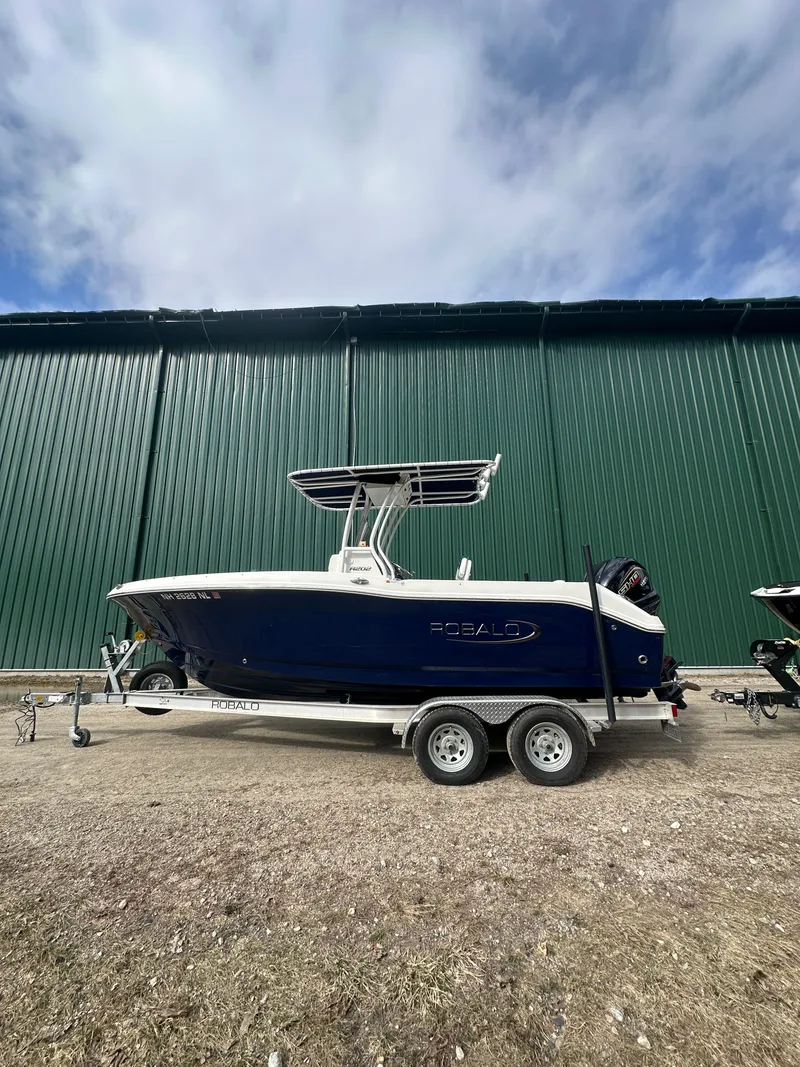 Slide: The Image of 2023 Robalo R202 Explorer boat on trailer in front of green building. - 2
