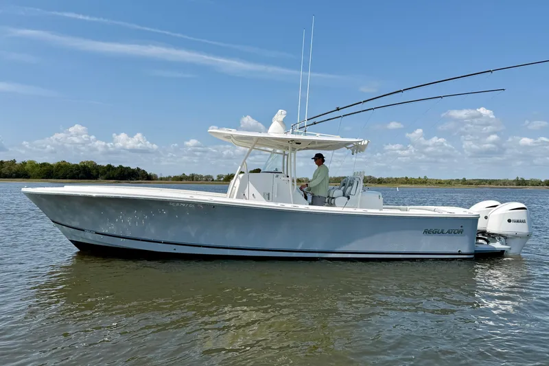 The Image of 2019 Regulator 31 boat on calm water, clear sky, person steering. - 0