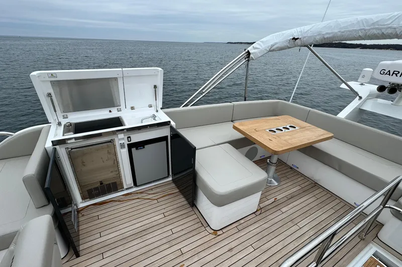 Slide: The Image of 2024 Fairline Squadron 50 yacht deck with seating, table, and kitchenette overlooking the ocean. - 64