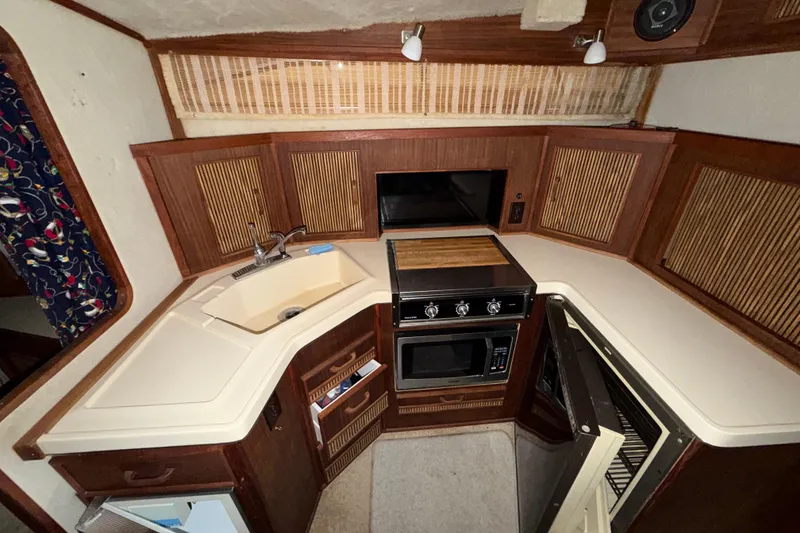 Slide: The Image of 1986 Sea Ray 340 Sundancer boat kitchen with sink, stove, and wooden cabinetry. - 18