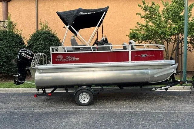 The Image of 2026 Sun Tracker Bass Buggy 16 XL Select pontoon boat on trailer, parked outdoors. - 0