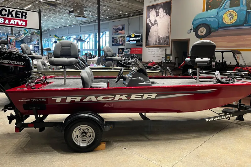 The Image of 2026 Tracker Pro 170 boat in showroom, red exterior, Mercury engine, displayed on trailer. - 0