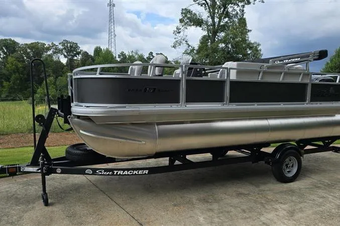 Slide: The Image of 2026 Sun Tracker Bass Buggy 18 DLX pontoon boat on trailer, parked outdoors. - 3