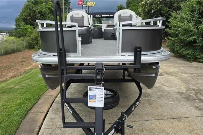Slide: The Image of 2026 Sun Tracker Bass Buggy 18 DLX pontoon boat on trailer, parked outdoors. - 2