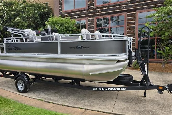 Slide: The Image of 2026 Sun Tracker Bass Buggy 18 DLX pontoon boat on trailer, parked outdoors. - 1