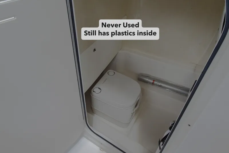 Slide: The Image of 2022 NauticStar 2302 Legacy boat interior with unused toilet, plastic wrap visible. - 18