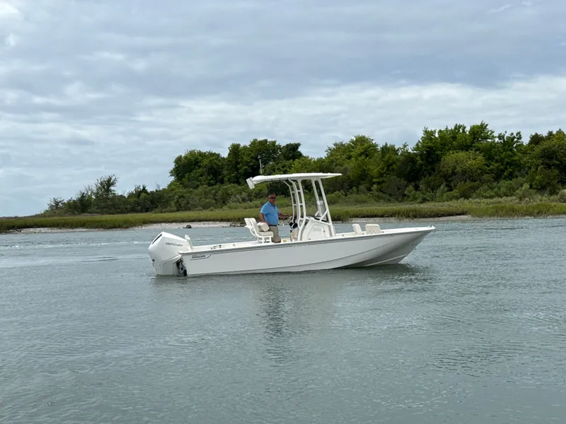 Slide: The Image of A 2026 Boston Whaler 210 Montauk on calm water. A man stands at the helm. - 0