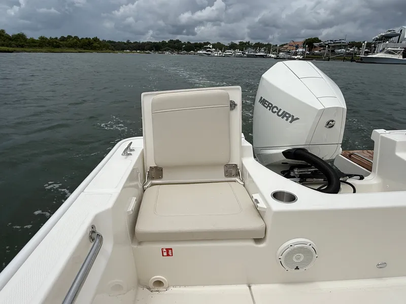Slide: The Image of A 2026 Boston Whaler 210 Montauk on the water. Visible is a seat and a Mercury engine. - 10