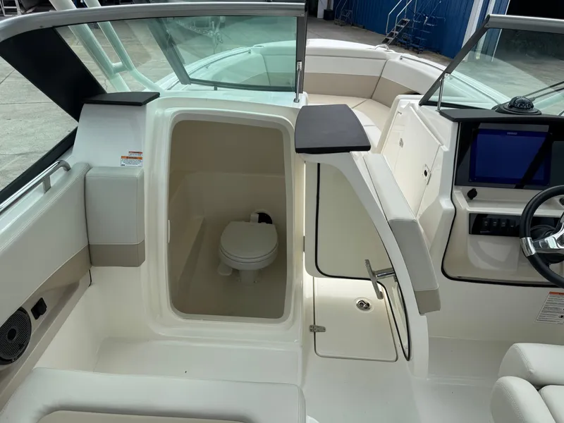 Slide: The Image of The image shows the cockpit of a 2027 Boston Whaler 240 Vantage. There's an open access to a toilet, surrounded by white upholstery and a modern helm with a screen. - 14