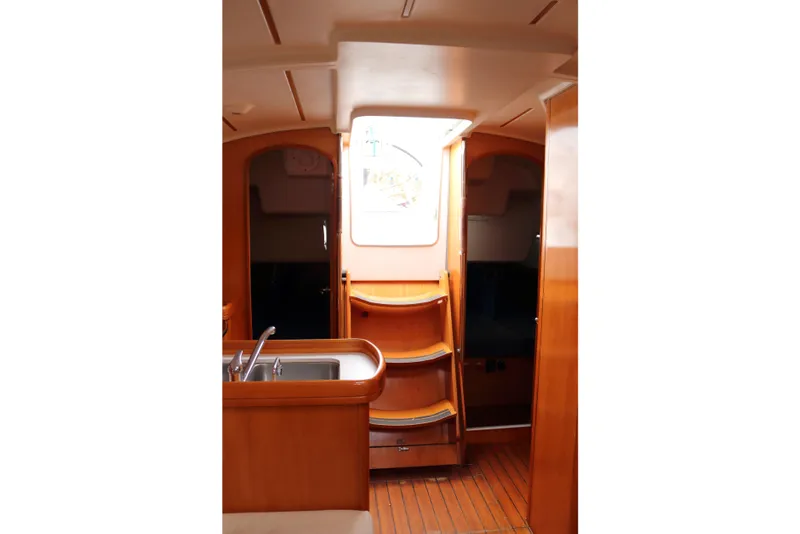 Slide: The Image of Interior of 2005 Beneteau First 47.7 yacht, featuring wooden cabinetry and a compact kitchen area. - 13