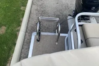 Slide: The Image of 2023 Sun Tracker SportFish 22 DLX boat ladder and seating area, parked on pavement. - 7