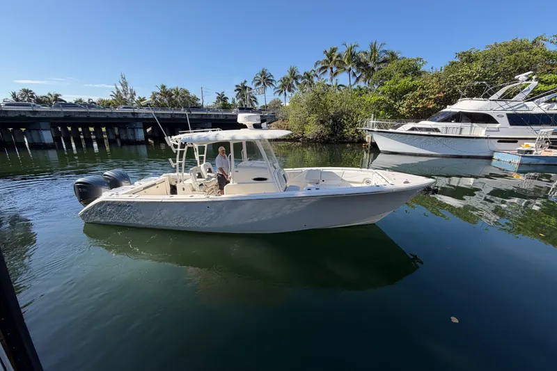 The Image of 2022 Cobia 320 Center Console boat on calm water near a bridge and palm trees. - 1